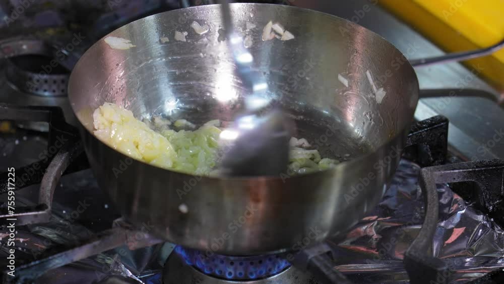 Professional chef in kitchen in restaurant cooking, fry onions in pan stirring frequently. Cooking in kitchen Sauteed onions stirred in pan with iron spoon. slow motion Professional chef in kitchen in restaurant cooking, fry onions in pan stirring frequently. Cooking in kitchen Sauteed onions stirred in pan with iron spoon. slow motion