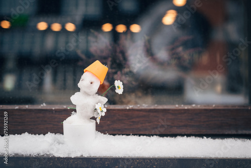 Fototapeta Naklejka Na Ścianę i Meble -  A small snowman with a chamomile flower on the windowsill of a street cafe.