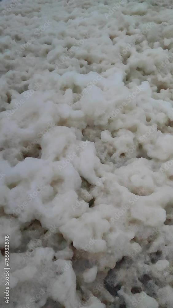 White foam from sea waves on a breakwater moving from the wind during a storm at dusk. Foam from the waves stirs on the pier in the sea. Vertical White foam from sea waves on a breakwater moving from the wind during a storm at dusk. Foam from the waves stirs on the pier in the sea. Vertical