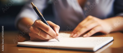 A woman is using office supplies to write in a notebook with a pencil. Her hand gestures as her thumb holds the pencil, creating art with every stroke of the writing instrument on the paper photo