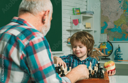 Grandfather and grandson child playing chess. Grandpa teaching grangson at chess school.
