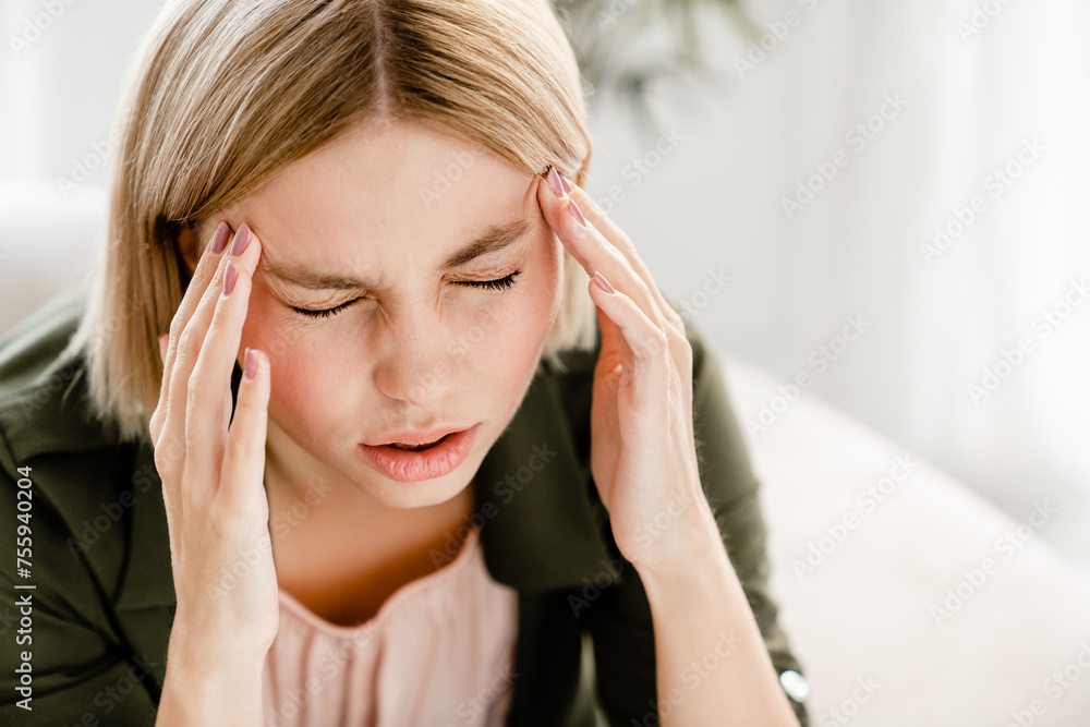 Sad caucasian woman having migraine rubbing temples. Young female girl suffering from headache, period crumps, having problems, being fired, crying at home Sad caucasian woman having migraine rubbing temples. Young female girl suffering from headache, period crumps, having problems, being fired, crying at home