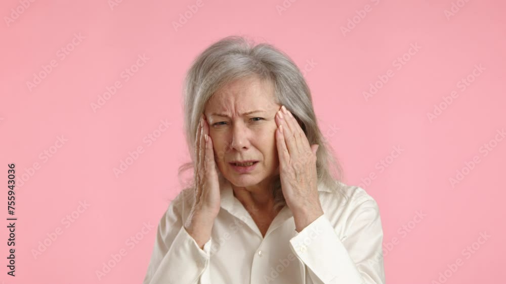 Mature woman squints, holding her head, struggling to see clearly, a sign of potential vision problems, standing against a minimalist pink backdrop. Camera 8K RAW. Mature woman squints, holding her head, struggling to see clearly, a sign of potential vision problems, standing against a minimalist pink backdrop. Camera 8K RAW.