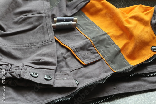 Workwear jacket with reflective stripes. Gray overalls with orange inserts. Spools of gray threads on the pocket of overalls © Nina