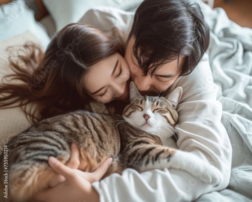 A man and woman sitting on a bed, cuddling with a cat.