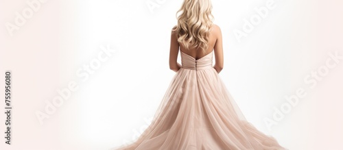 A woman in a long pink wedding gown is standing in front of a white background, her hair cascading over her shoulders like a doll in bridal clothing