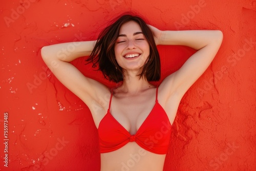 A cheerful woman strikes a pose in a red bikini against a striking red wall backdrop