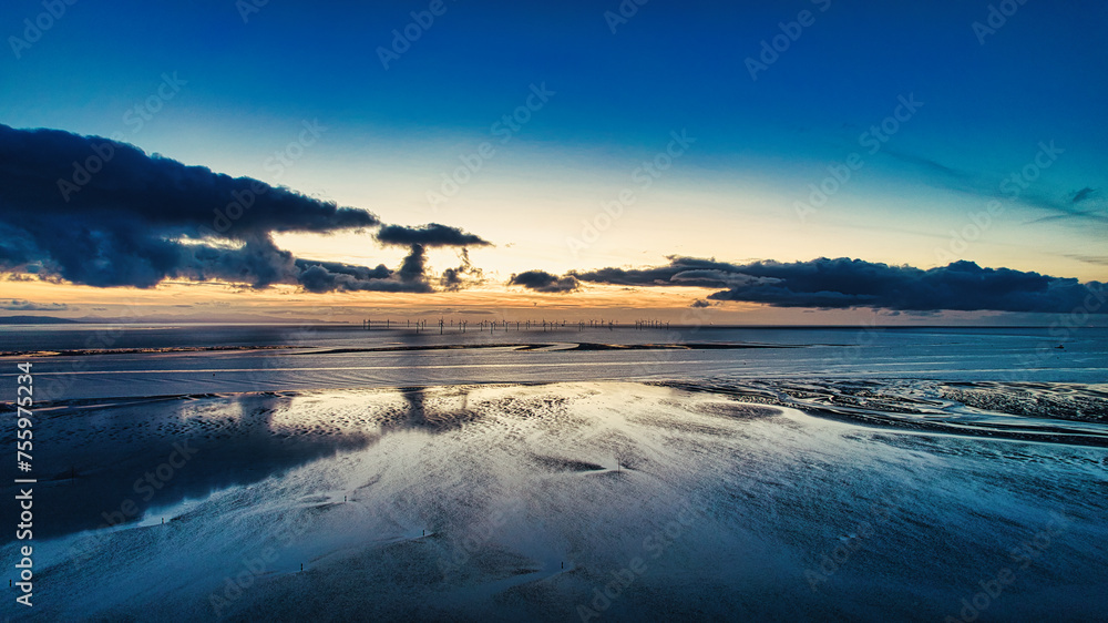 Tranquil beach sunset with reflections on water and dramatic clouds in Crosby. UK.