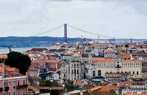Panoramic view of the cityscape of Lisbon, Portugal, with Sao Jorge Castle and the red roofes of the Alfama district until the Tagus river on a sunny day. Blue sky. April 25 Bridge