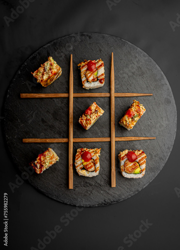 Sushi on a round black volcanic plate in a tic-tac-toe style.