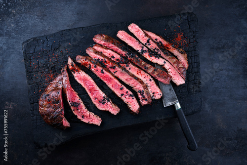 Traditional barbecue wagyu gourmet flank steak sliced with black salt and chili served as top view on a charred wooden design cutting board