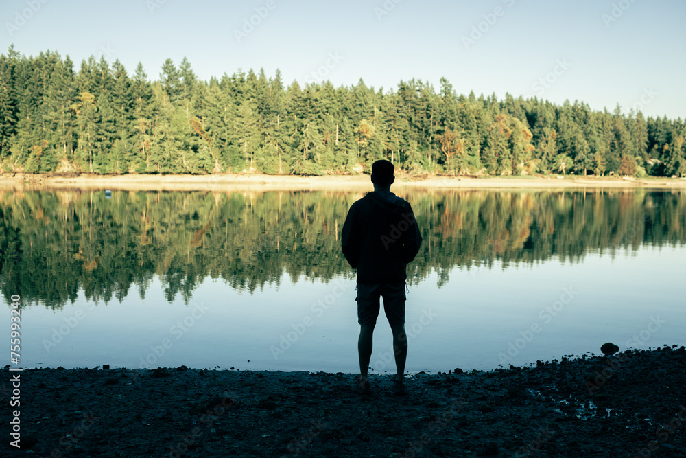 Silhouette of thoughtful man stand by a lake alone in nature 
