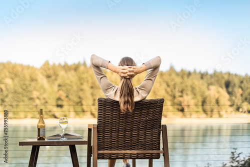 Young happy woman sitting back relaxing enjoying time in nature, wine, book on a summer day #755993880