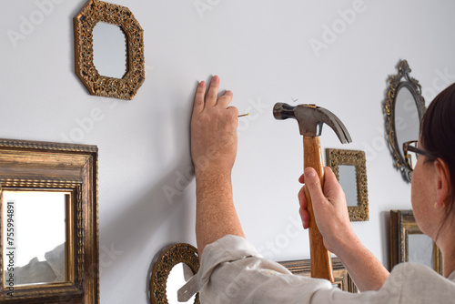 Closeup woman is putting nail in a wall with a hammer to hang mirrors in a gallery style photo