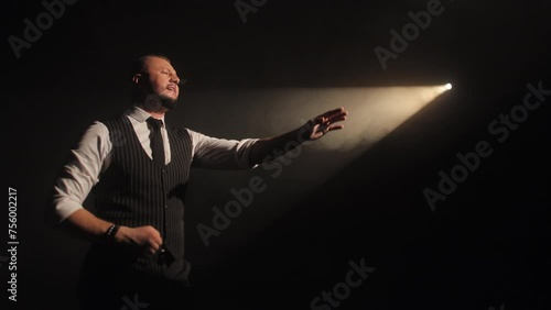 Actor in elegant suit and tie performing in contrast lighting and expressing personal emotions with hand gesture. Creative man singing beautiful song about love on scene in dramatic atmosphere. photo