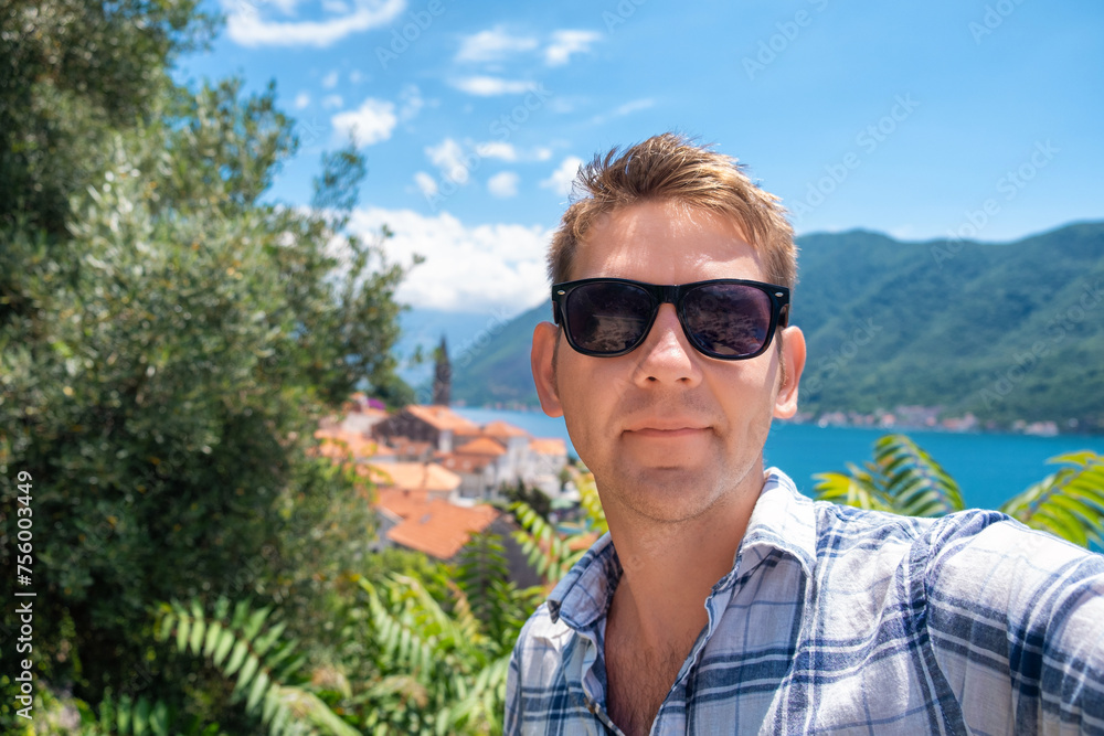 Man tourist in sunglasses take a selfie with old town Perast in Kotor bay, Montenegro on background. Handsome male traveler on summer vacation taking selfies with landmark for social media Man tourist in sunglasses take a selfie with old town Perast in Kotor bay, Montenegro on background. Handsome male traveler on summer vacation taking selfies with landmark for social media