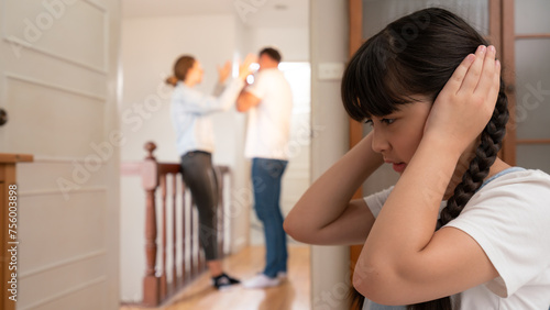 Stressed and unhappy young girl huddle in corner, cover her ears blocking sound of her parent arguing in background. Domestic violence at home and traumatic childhood develop to depression. Synchronos © Summit Art Creations