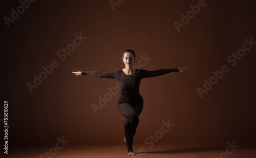 woman in yoga pose on brown background in brown sports overalls