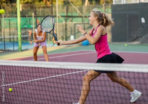 Sporty teenager girl player hitting ball with racket on court during friendly doubles couple match © JackF