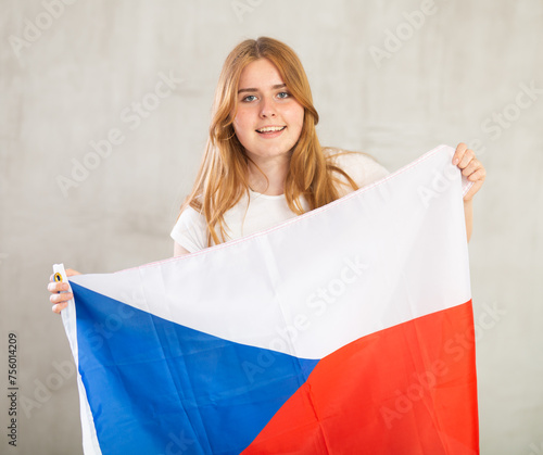 smiling girl holds canvas of Czech flag in front of her. Gray background. Unity of nation and independence