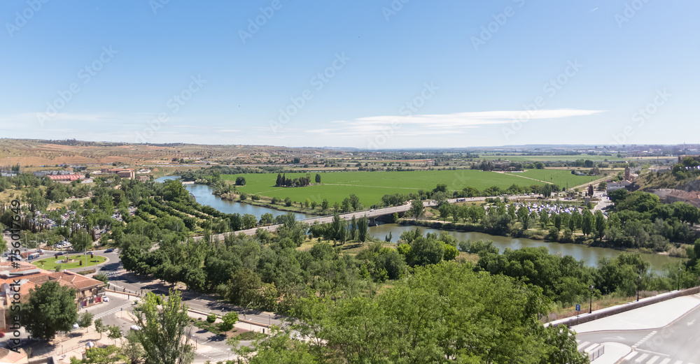amic aerial view of the outskirts of the city of Toledo, parks with trees, Tagus river or Tejo river, agricultural fields and horizon, in Spain
