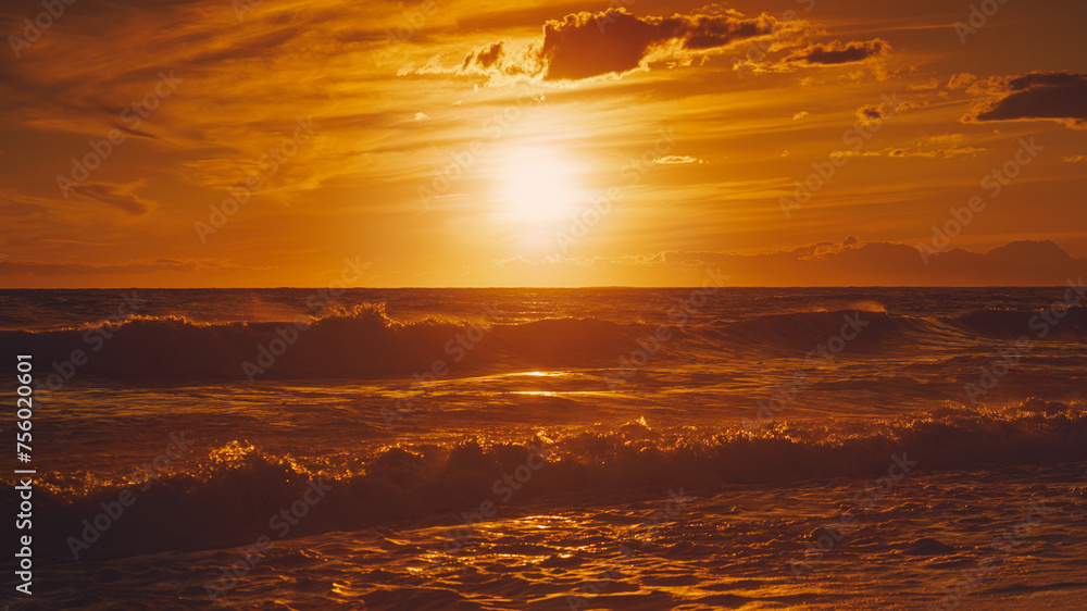 Fototapeta premium Alanya, Antalya, Türkiye, Turkey, Panoramic view of the undulating Mediterranean Sea with waves at sunset, bright orange sun in the sky and clouds around