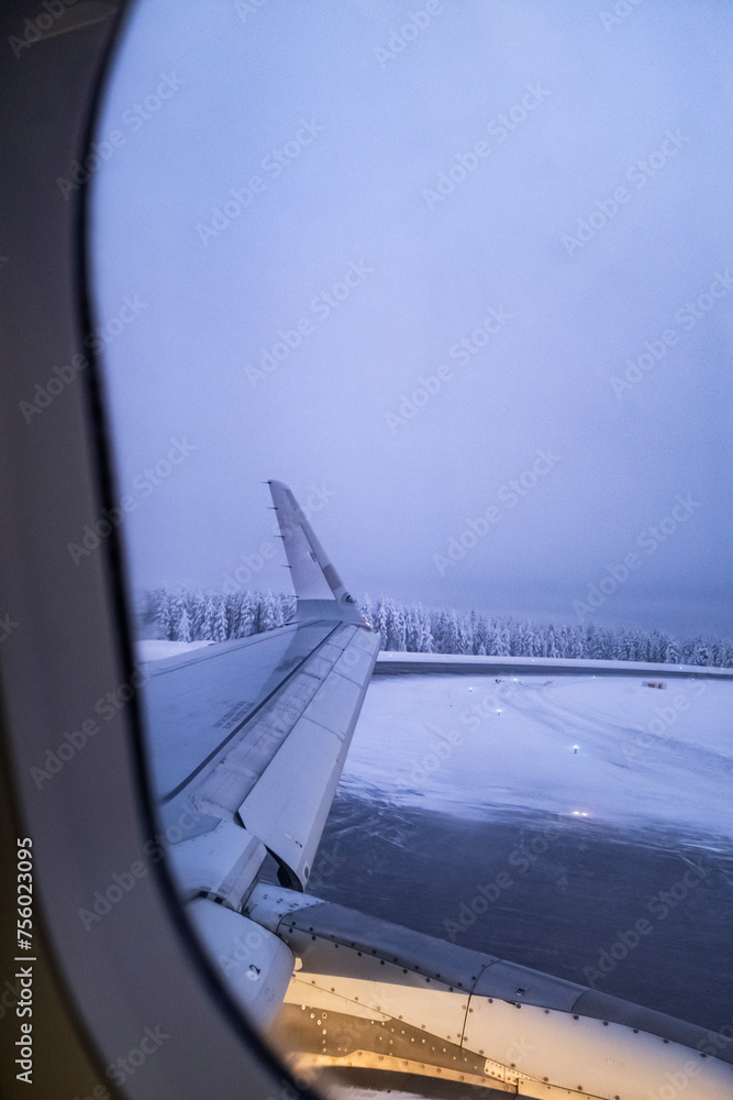 Airplane window scene while taking off on a snowy white track airport landscape