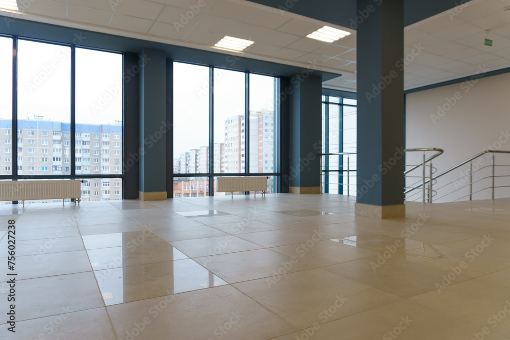 Fototapeta premium An empty spacious room of a modern office building with large windows. An empty hall with columns and a new renovation. Interior design. Suspended ceiling and square LED lamps.