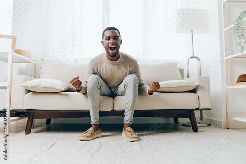 Thinking Man Resting on Comfortable Sofa in Modern Living Room, Smiling and Happy African American Young Adult Enjoying Relaxation and Technology, Holding Laptop, Alone at Home