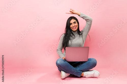 Excited young woman using the laptop and making the peace sign