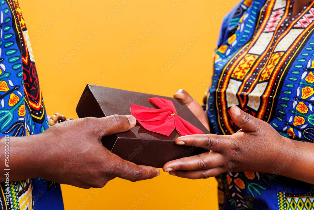 Black couple exchanging anniversary gift, holding in hands wrapped box with bow ribbon closeup. African american man and woman sharing festive present, receiving box close view