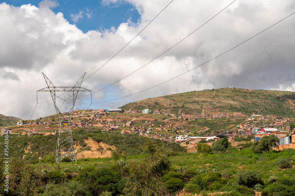 electricity pylons installed in a rural area with houses built on a hill in the background
