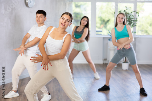 Female teenager performs movements during warm-up, limbering-up part of workout together with peers. Group of young girls and guy engage modern house dance in fitness club.