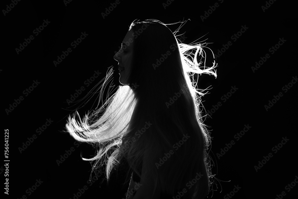 Fototapeta premium Silhouette of young woman with waving hair on black background
