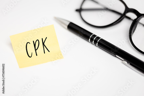 A yellow sticky note on a white background with the handwritten inscription "CPK", next to it a black pen and glasses (selective focus)