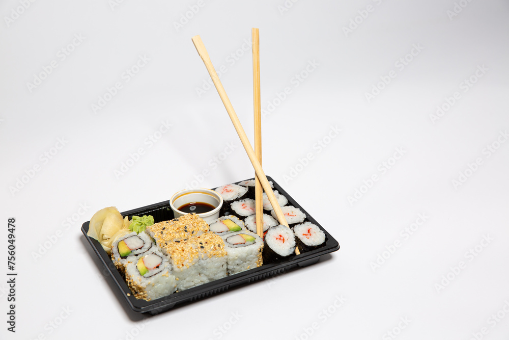 Sushi to go in a black takeaway box with wooden chopsticks on white background Sushi to go in a black takeaway box with wooden chopsticks on white background