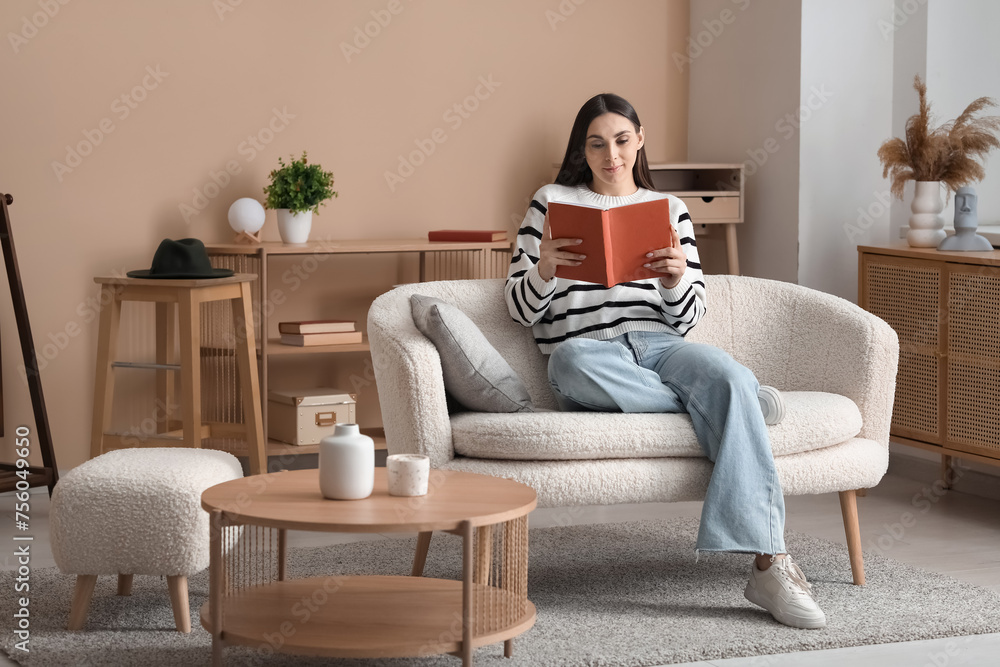Beautiful young woman sitting on comfortable sofa and reading book in living room at home Beautiful young woman sitting on comfortable sofa and reading book in living room at home