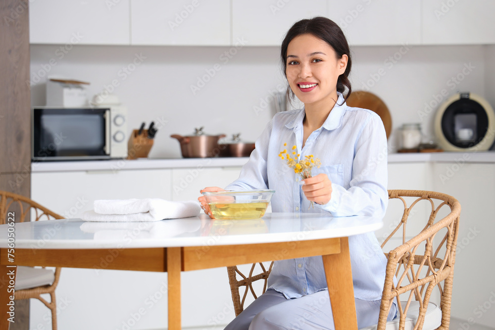 Young Asian woman preparing steam inhalation with herbs at table in kitchen Young Asian woman preparing steam inhalation with herbs at table in kitchen