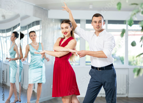 Expressive young adult woman in elegant vibrant red dress dancing passionate bachata with male partner during dance class for adults led by female instructor..