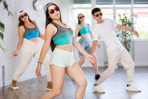Group of young women and young guy in sunglasses rehearsing hip hop dance in dance studio