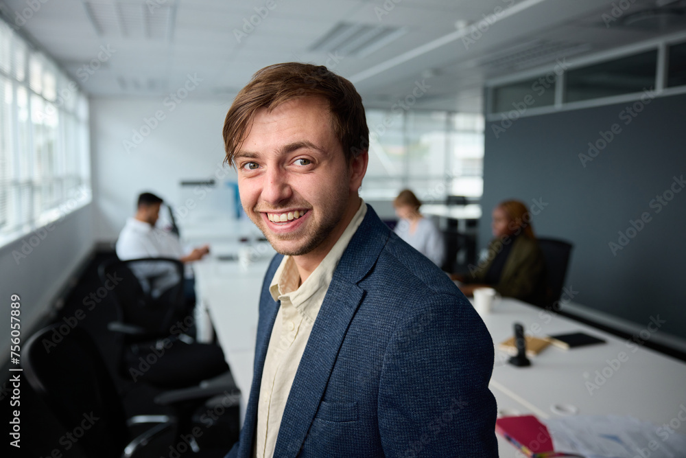 Confident young businessman in businesswear with next to desk with coworkers in office