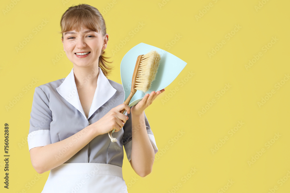 Young chambermaid with dustpan and brush on yellow background Young chambermaid with dustpan and brush on yellow background