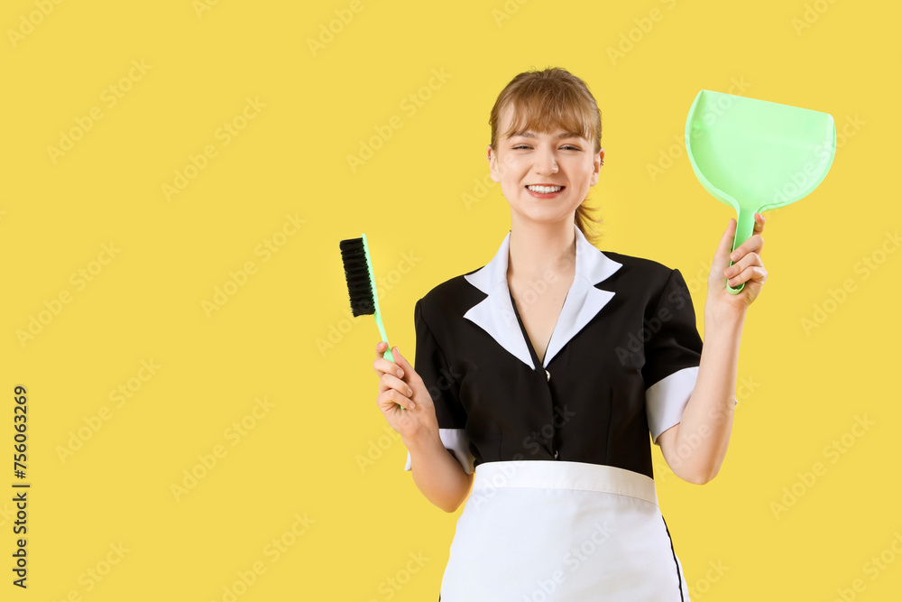 Young chambermaid with dustpan and brush on yellow background Young chambermaid with dustpan and brush on yellow background