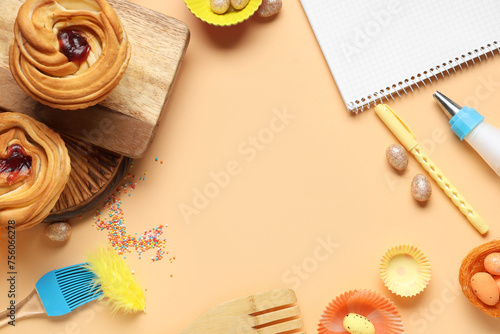 Frame made of blank notepad for recipes with sweet buns, Easter eggs and baking tools on beige background