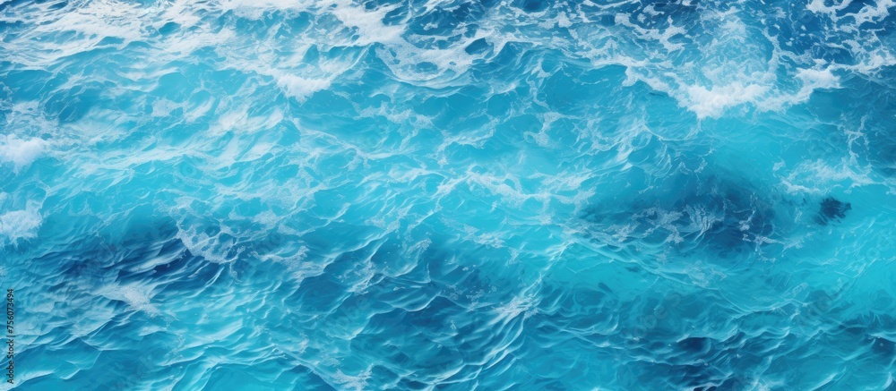 A close up of the electric blue ocean with waves crashing on the shore, creating a beautiful pattern. The water is fluid and the wind waves are perfect for recreation