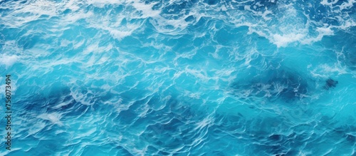 A close up of the electric blue ocean with waves crashing on the shore, creating a beautiful pattern. The water is fluid and the wind waves are perfect for recreation