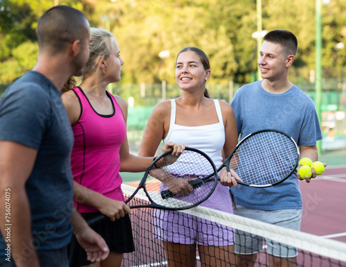 Group photo of positive people standing on tennis court after another game and having conversation. © JackF
