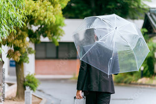 梅雨・台風の雨でビニール傘をさす外国人ビジネスマン 
