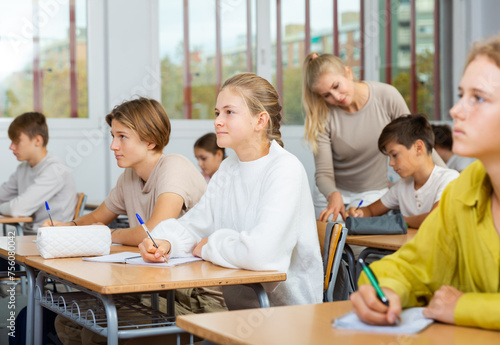 Teen boys and girls sitting at desk in classroom full of pupils during lesson