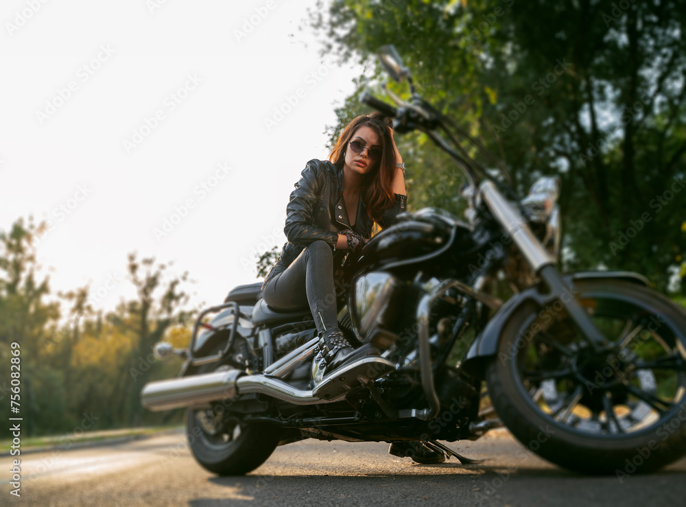 Fototapeta premium Amazing powerful girl sitting on vintage motorcycle parked on the road and looking seriously at camera 